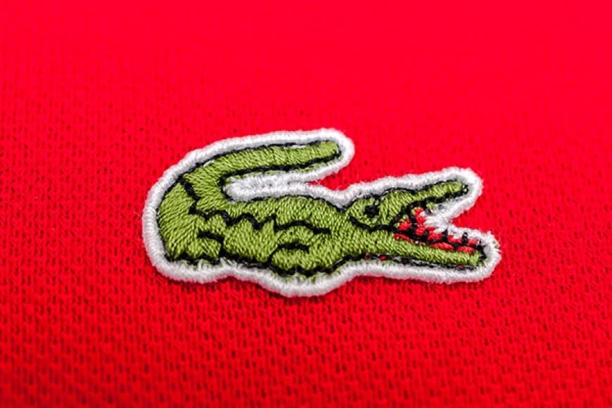 Inkomoko y'akamenyetso k'ingona (crocodile) kagaragara ku mipira yitwa Lacoste
