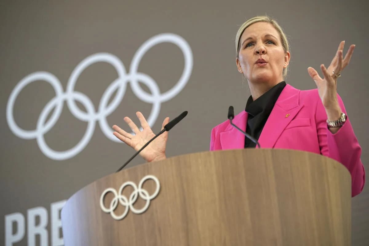 Kirsty Coventry stands at a lectern in front of a projection of the five interlocking rings that signify the Olympics.