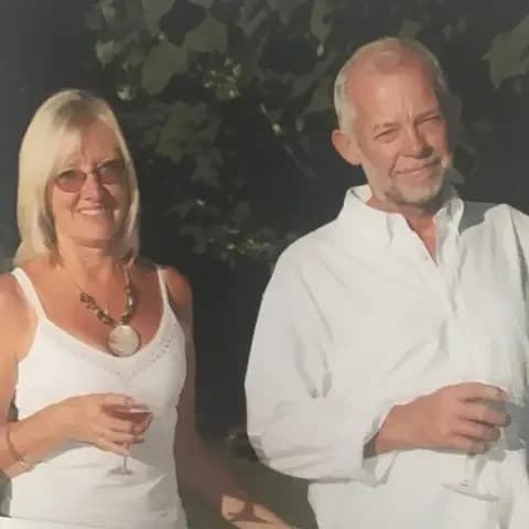 Family handout Margaret Manion wears a white top and stands with her partner against a green background, in sunshine. /BBC
